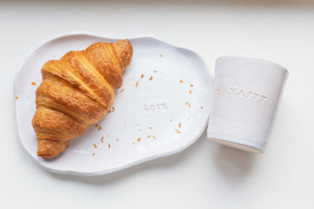 White plate and glass made of handmade clay with fresh croissant on a white tableの写真素材