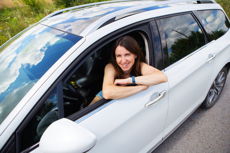 Young girl driving a car, the girl looks in the side mirror and smiles. Delivery for the right to drive a carの写真素材