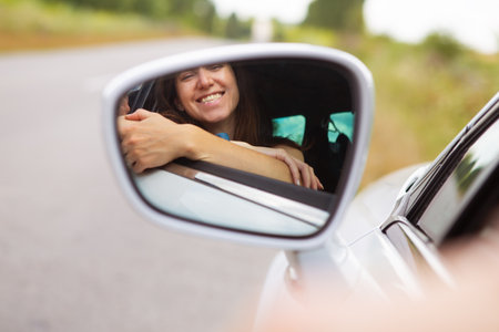 Young girl driving a car, the girl looks in the side mirror and smiles. Delivery for the right to drive a carの写真素材
