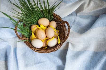 Beautiful painted Easter eggs, one egg with a cute face, eggs lie in a wooden basket along with green grass. easter postcardの写真素材