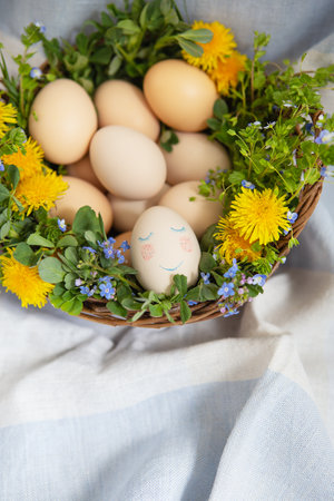Beautiful spring bouquet in a wooden basket with Easter painted eggs, eggs with cute faces. Easter colorful card. View from aboveの写真素材