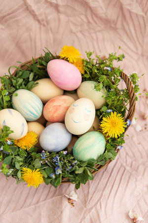 On a pastel cover a basket with herbs and bright flowers. The basket contains Easter eggs painted in watercolor in beautiful pastel colors. Great Easterの写真素材