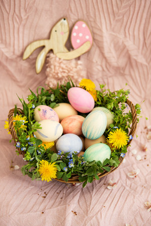 On a pastel bedspread is a basket of grass and various bright flowers, a rabbit. The basket contains Easter eggs painted with watercolors in beautiful pastel colorsの写真素材
