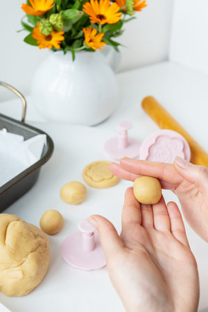 Preparing the dough for making cookies with molds in the form of flowers, a rolling pin, a bouquet of orange flowers and a baking sheet, the girl forms cookies in her hands. concept of family and cookingの写真素材