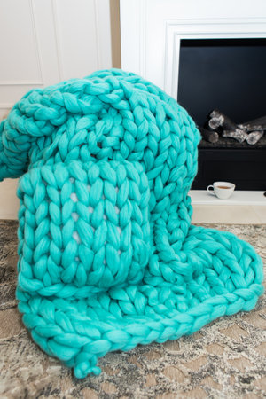 A warm plaid knitted from merino wool of a beautiful aquamarine shade lies near the fireplace along with a cup of tea. The concept of comfortの写真素材