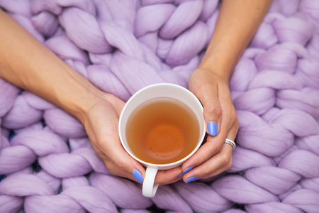 A girl wrapped in a large pink merino wool blanket, a warm and very soft blanket, a girl holding a cup of hot white tea, top viewの写真素材