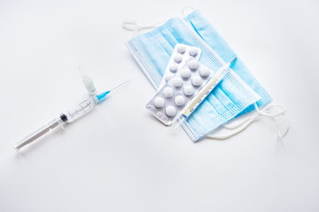Preparation for vaccination against covid-19. Thermometer, pills, medical mask on a white table. Place for an inscription, horizontal photoの写真素材