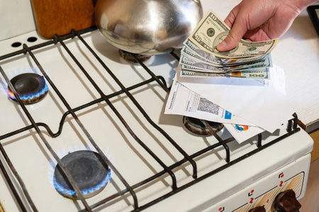Payment of utility services. Dollar bills, utility bills are held in their hands near a burning gas...
