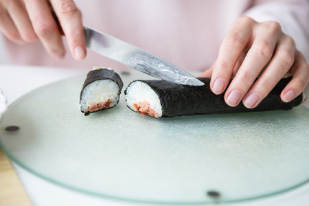 The process of making sushi, the girl makes sushi with different flavors - fresh salmon, caviar, avocado, cucumber, ginger, rice. Cut the roll into pieces. close-upの写真素材