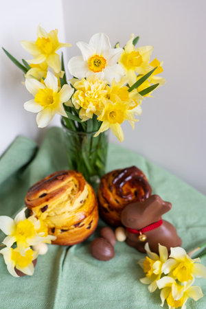Homemade Easter traditional pastries lie on a green napkin along with daffodil flowers, rabbit, chocolate eggs. Easter baking and decor, vertical photoの写真素材