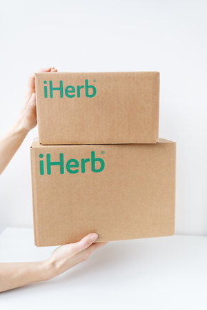 Kyiv, Ukraine-December 17, 2022: . IHerb box packaging in the hands of the courier, fast delivery to the door. Online ordering, delivery of goods and vitamins for healthの写真素材