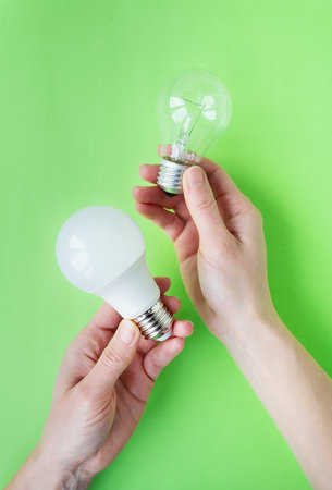 A set of two types of lamps, LED and incandescent, in the hands of a girl isolated on a green background. energy-saving lampsの写真素材