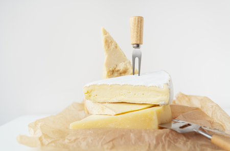 Different types of cheese lie on top of each other with cheese knives on parchment. A delicious delicacyの写真素材