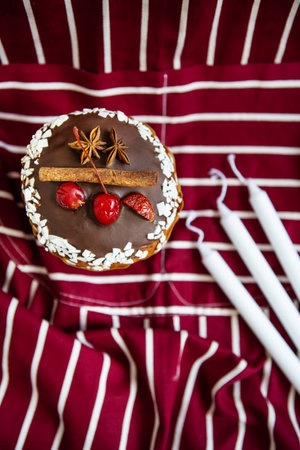 A traditional paska decorated with white and dark Swiss chocolate and cherries, cinnamon and star anise stands on a cherry striped apron. Easter holiday, top viewの写真素材