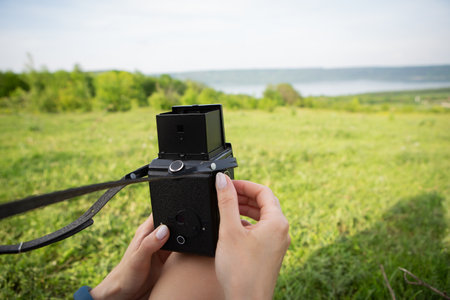 Photo of the hands of a young photographer with an old camera shooting a very beautiful landscape of a lake and a green meadowの写真素材