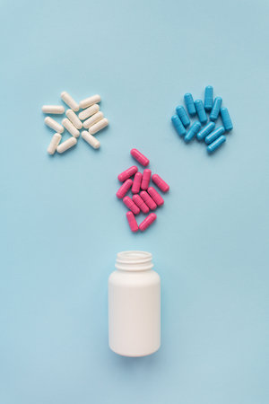 Various multicolored bright capsule pills flying from an open plastic bottle isolated on a blue background. The concept of evidence-based medicine and healthcareの写真素材