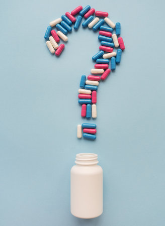A question mark consisting of three multi-colored vitamins on a blue background along with a plastic white vial. Health problems and treatment. The concept of evidence-based medicineの写真素材