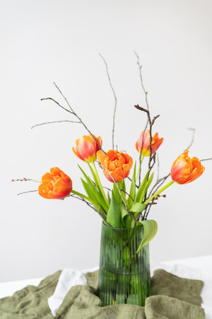 A very beautiful spring bouquet in a green vase stands on a table on a linen tablecloth, orange peony tulips. Mother's Day, March 8, Valentine's Dayの写真素材