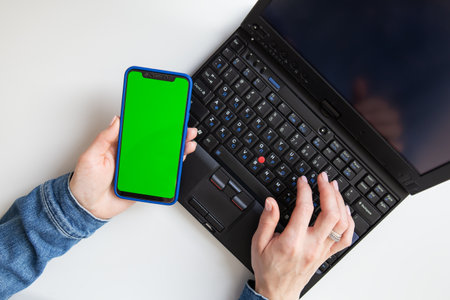 The girl is working on a laptop. Freelance, remote work, hands on the keyboard, in one hand a smartphone with a green screen. Mocap. View from aboveの写真素材
