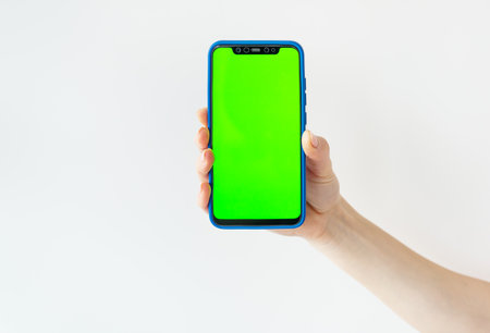 Mockup image, girl holding smartphone with blank green screen on white wall. Ready mockup for designersの写真素材