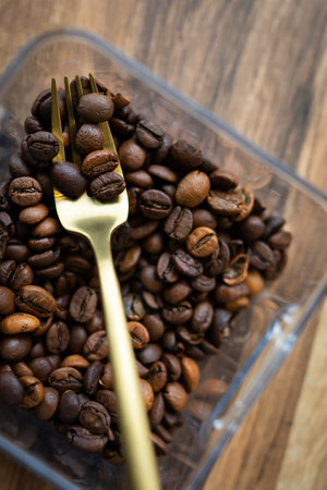 Roasted coffee bean in a plastic box along with a fork, close-up, top view. The concept of making coffeeの写真素材
