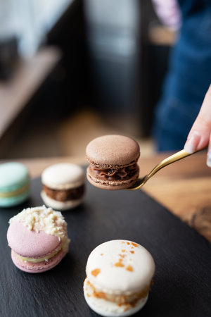 A delicious macaron dessert - a French sweet delicacy lies on a concrete black stand, and a girl holds a candy with a fork. vertical photoの写真素材
