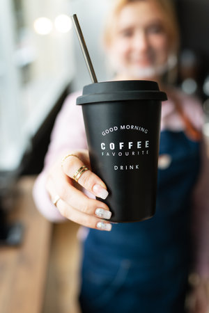 Barista girl holding a black metal glass with the inscription good morning favorite coffee drink in her hands with prepared hot coffee. professional coffee preparationの写真素材