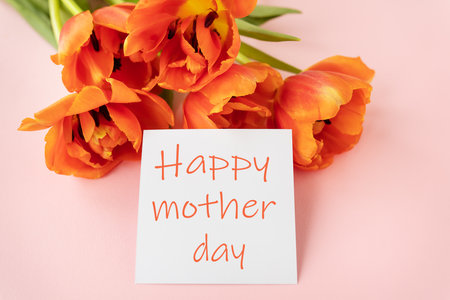 A beautiful bouquet of orange peony tulips along with a white card in the middle with the words happy mother day on a pink backgroundの写真素材