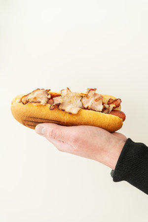 Cropped view of young guy holding tasty hot dog with mustard and ketchup on white background. Street food, deliveryの写真素材