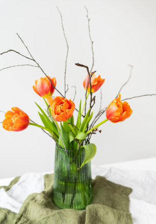 A very beautiful spring bouquet in a green vase stands on a table on a linen tablecloth, orange peony tulips. Mother's Day, March 8, Valentine's Dayの写真素材