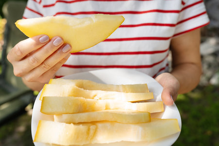 A girl in a striped T-shirt holds a piece of yellow juicy melon in her hands. Summer, rest, travelの写真素材