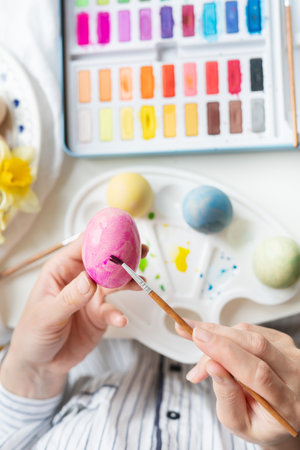 A brush in the process of painting Easter eggs with watercolors. top view, vertical photoの写真素材