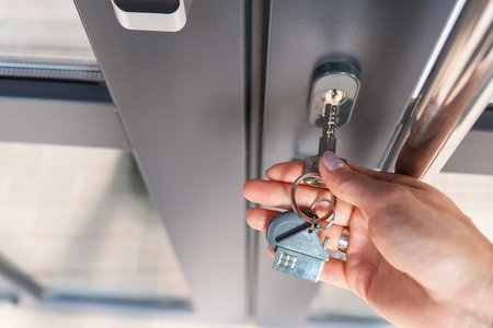 A woman's hand opens the door with a key on which the keychain hangs at homeの写真素材