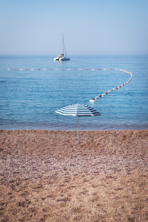 The famous resort island of St. Stephen in the Adriatic Sea, Montenegro. The concept of sea holidays, a yacht in the sea, a striped umbrella stands on a sandy beachの写真素材