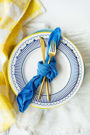 Gold cutlery is tied with a blue napkin, on which the plates are on a green-yellow linen napkin. Minimalist design, rustic. Birthday or wedding celebration. Serving designの写真素材
