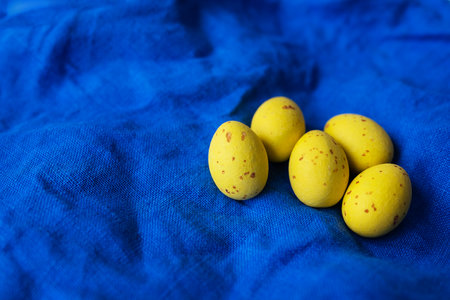 Top view of yellow decorated Easter eggs on napkin on blue textured linen background. Easter concept, place for inscriptionの写真素材