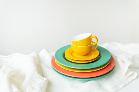 Empty yellow cups and brightly colored plates on a white table covered with a linen tableclothの写真素材