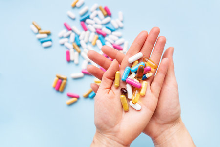 The girl holds a handful of bright vitamins in her palms against the background of other bright capsules. Concept of medicine and healthcareの写真素材