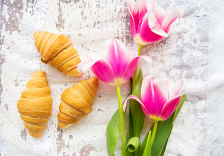Three croissants and bright pink tulips on lace tablecloth.の写真素材