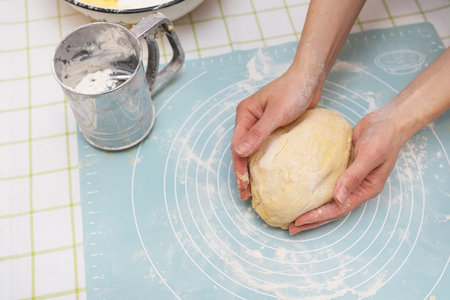 A woman kneads the dough with her hands, the hands of a baker, a silicone mat, a sieve, handmade baking. View from aboveの写真素材