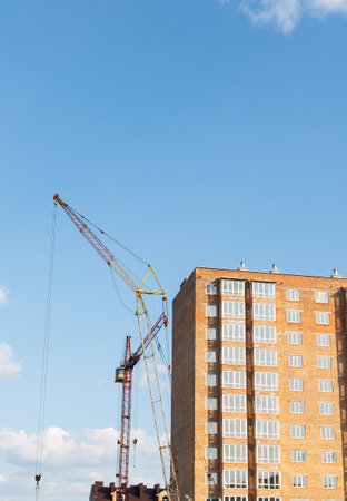 Construction of a new apartment building, against the blue sky, a high-rise construction crane. vertical photoの写真素材