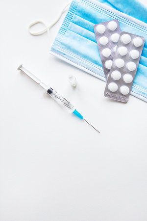 Preparation for vaccination against covid-19. Thermometer, pills, medical mask on a white table. Place for an inscription, vertical photoの写真素材