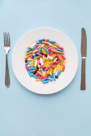 Tablets, capsules, vitamins and natural organic food supplements on a white plate on a blue background. Minimal modern pharmacy or healthcare concept. vertical photoの写真素材