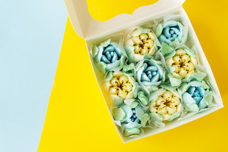 Yellow-blue marshmallow in the form of flowers in the form of tulips. Marshmallow in a box on a yellow-blue background. View from aboveの写真素材