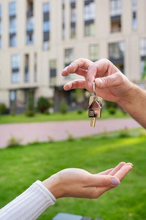Keys with a keychain in the form of a metal house from a new house or apartment in the hands of a young family. Happiness from buying a house. Handing over the keys from the realtorの写真素材