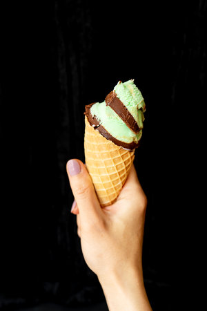 Summer, vacation, ice cream. The hand holds soft ice cream in a chocolate-mint waffle cup. On a black background, close-upの写真素材