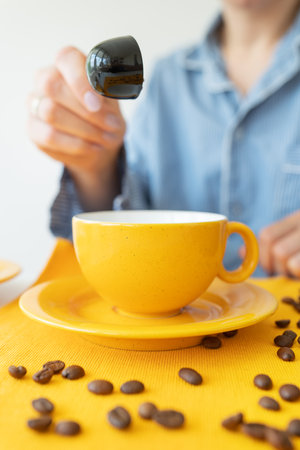 A young woman prepares herself coffee in a bright yellow mug. Grains of coffee on the table. Enjoy fresh aromatic coffeeの写真素材
