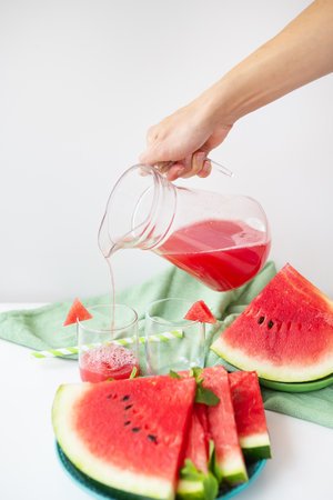 Close-up of fresh watermelon juice or smoothie in glasses with watermelon slices on a white table. A refreshing summer drink is poured into glassesの写真素材