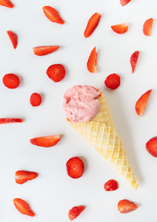 Strawberry ice cream in a waffle cup in the form of a cone, ice cream lies on a white table along with slices of fresh strawberries. vertical photoの写真素材