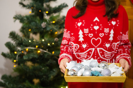 Female hands hold a tray in which there are a lot of Christmas tree toys. Christmas tree decoration process. New Year Christmas. 2022 year of the tigerの写真素材